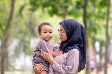 Fototapeta premium image of an asian mother and baby having fun in the park. Mother and baby playing in the park at the sunset time. Family, trust, protecting, care, parenting, summer vacation concept.