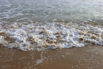 Soothing waves crashing on shore of sandy beach on a cloudy Day