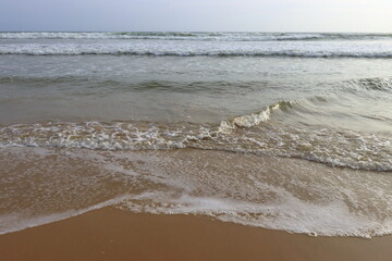 Soothing waves crashing on shore of sandy beach on a cloudy Day