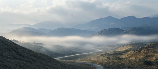 Misty mountain road winding through valleys and hills at sunrise.