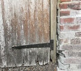 Black metal hinge on old rotting gate with brick wall to the side