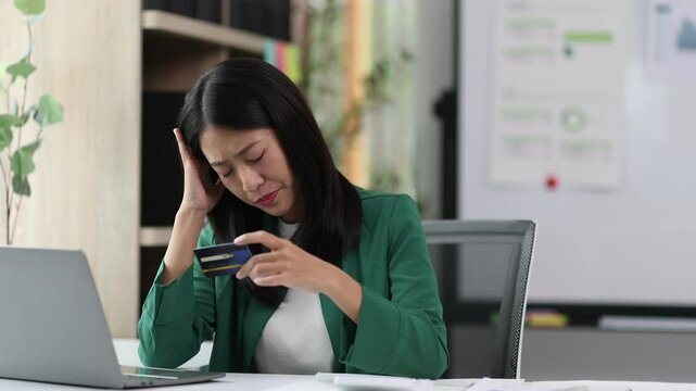 Stressed young woman overwhelmed by financial debt. Young businesswoman feeling financial debt stress, holding credit card and frustrated while working office desk.