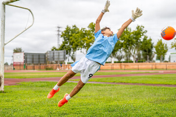 Focused soccer goalkeeper leaping mid-air, blocking orange ball during intense training session on...