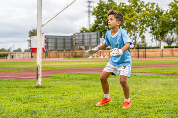 Young goalkeeper wearing gloves is waiting to save a goal during a soccer match on a grassy field, demonstrating concentration, agility, and anticipation in the face of upcoming action