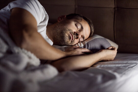 Young man sleeping deeply and dreaming in dark bedroom at night.