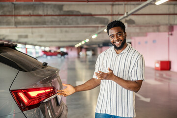 Young black casual man is presenting his classy car while standing at garage.