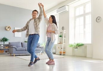 Happy overjoyed laughing young couple homeowners having fun dancing at home in living room celebrating moving into new apartment or enjoying a good mood and happy life moments together.