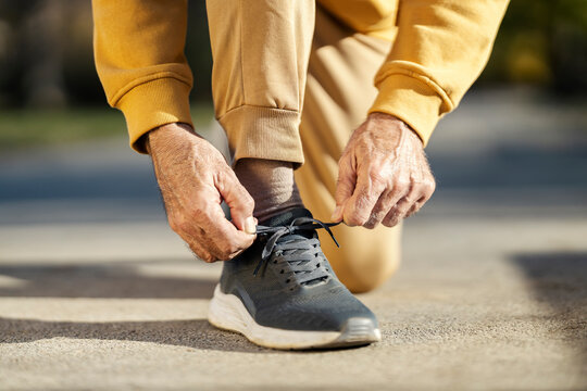 Close up of active senior man's hands tying shoelace on sneaker and preparing for outdoor fitness.