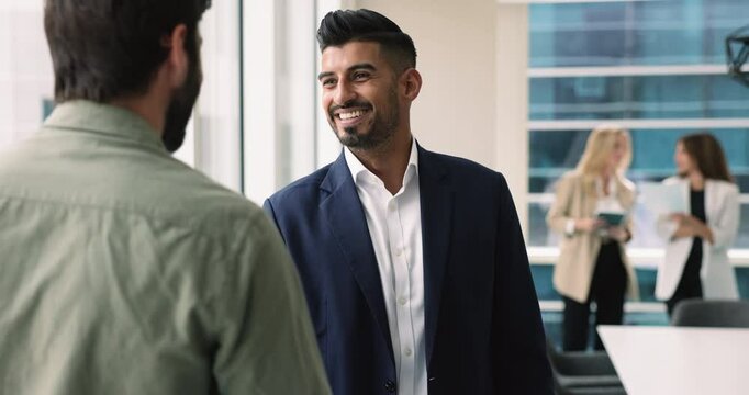 Happy confident handsome Indian businessman in formal suit shaking hands with company client, male business partner, colleague, smiling, thanking for partnership, saying good bye after meeting