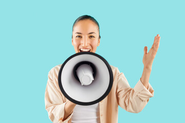 Studio shot of happy young Asian woman screaming in megaphone. Cheerful young girl isolated on bright blue background holding loud speaker in hand, looking at camera and talking with amplified voice