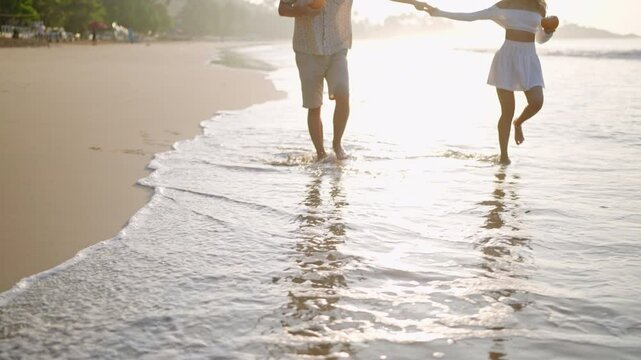 Man, woman in love walk barefoot in sea surf water edge. Reflection of couple with coconut cocktails on wet beach sand. Shadow of people going on ocean coastline waves. Lovers hold hands on vacation.