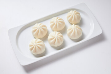Steamed bao buns in a white rectangular plate on a white plain background.