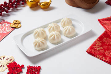 Steamed bao buns in a traditional bamboo steamer on a white plain background. With traditional and oriental decoration surrounding it.