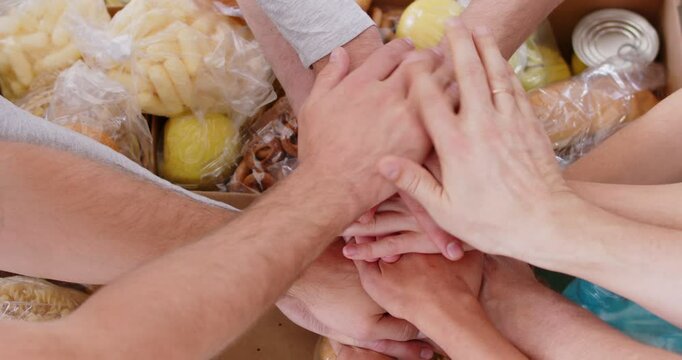 Group of volunteers fold their hands in triumph over food that was donated for community program. Volunteers work harmoniously together to ensure that those in need have access to nutritious food.