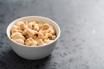 Dry cashew nuts in white bowl on concrete background with copy space