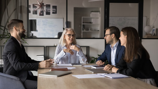 Employees listen to mature leader, discussing strategy, making speech take part in morning briefing in company boardroom. Mentor explaining corporate goal, giving instructions to workers at meeting