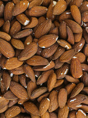 A close-up image of a large pile of almonds. The almonds are a light brown color with some visible skin and a few cracks.