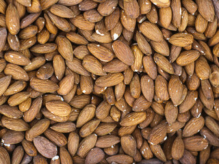 A close-up image of a large pile of almonds. The almonds are a light brown color with some visible skin and a few cracks.