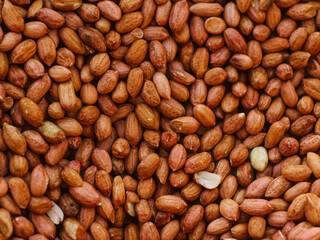 A close-up image of a large pile of unshelled peanuts. The peanuts are a rich, reddish-brown color with visible veins and some slight cracking. 