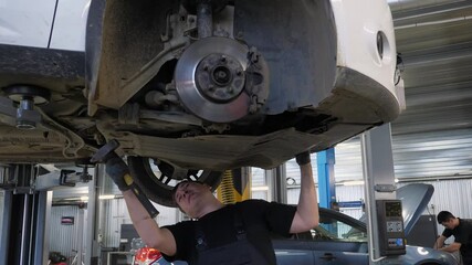 An auto mechanic working under the car on a car lift in the garage, he disassembles the bottom of the car for further repair. Antifreeze drain in the service station. Auto repair shop, auto repair.