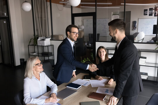 Group of shareholders greeting each other before negotiation in modern conference room, shaking hands, expressing mutual respect, thanking for successful collaboration and future partnership in office