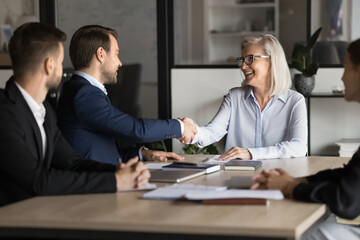 Business parts conclude partnership, finalizing formal meeting negotiations in boardroom with handshake gesture of trust, mutual respect and agreement. Mature and young shareholders greet each other