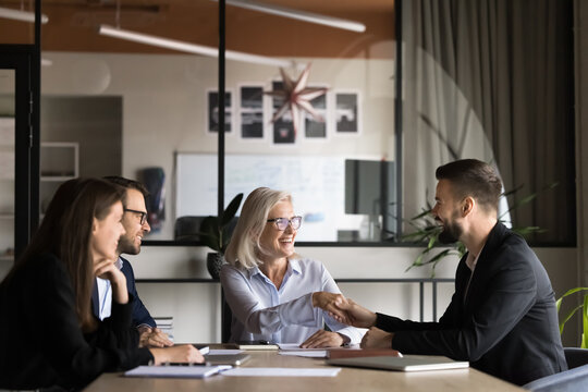 Business parties, shareholders gathered together sit at conference table finish negotiations after signing contract, shaking hands, gesture of closing successful profitable deal, expressing respect