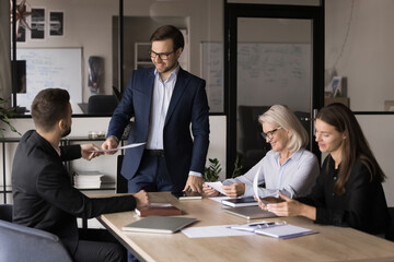 Millennial boss in suit holding meeting with business team, giving papers to negotiation member...