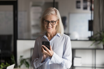 Smiling businesswoman looking at her smartphone, enjoy online chat by business or personal, checking e-mails working, communicating for professional reasons in modern workplace. Modern tech, workflow