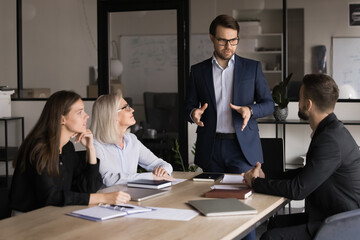 Businessman dressed in suit explaining or presenting information, standing in front of group of...