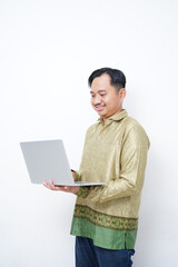 Adult Asian man wearing batik smiling while using his laptop - Indonesia men