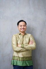 Confident adult Asian man wearing traditional batik with arms crossed - Indonesian culture portrait