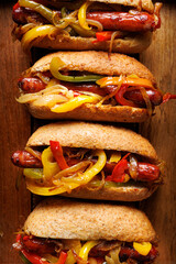 Sausage sandwiches with colorful peppers and onion on a wooden background, focus on the middle, close up view. Hot dog form with added vegetables