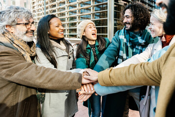 Group of business people stacking hands over corporate office building. Unity, teamwork, partnership and cooperation concept.
