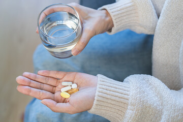 Sick, asian young woman, girl hand holding pill capsule, painkiller medicine from stomach pain, head ache, pain for treatment, take drug or vitamin and glass of water at home, pharmacy and health care