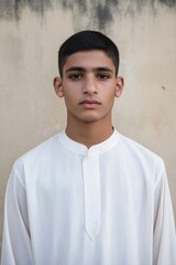 Obraz premium A young man wearing a white shirt and a white scarf stands in front of a wall. He has a serious expression on his face