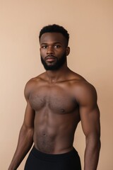 Fototapeta premium A man with a shaved head and a beard stands in front of a tan wall. He is wearing black shorts and a black shirt