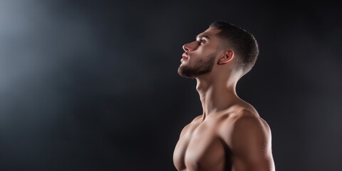 Fototapeta premium A man with a beard and a shaved head is standing in front of a dark background. He is looking up at something