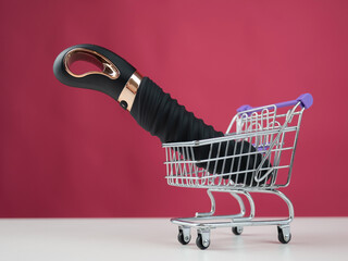 Sex toy in miniature shopping cart on pink background. 