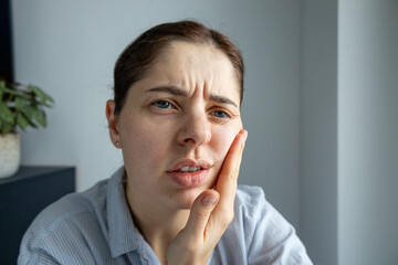 Portrait of a young woman holding her cheek, expressing discomfort or dental pain