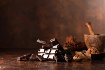 Broken dark chocolate bar and cocoa powder on a brown table.