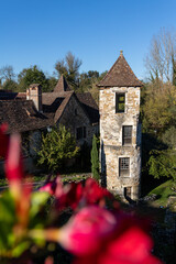 Historic Tower and Stone Buildings in Carennac, France with Vibrant Floral Foreground