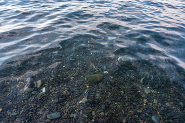 Underwater pebble backgrounds. Colorful stones sea bottom in the sun rays. View from above through clear water. Seascape wallpaper texture. Defocus.