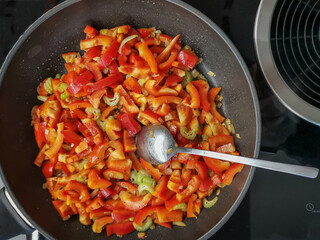 Colorful bell peppers and celery sautéing in a pan on a stovetop in a home kitchen