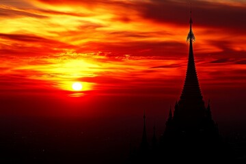 Obraz premium Majestic Silhouette of a Tower Against a Vibrant Sunset with Orange and Red Hues Illuminating the Sky Overlooking a Scenic Landscape