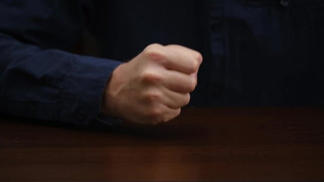 close-up male hand lying on table, slowly clenching into fist and knocking hard on table. hand gesture disappointed, angry businessman.