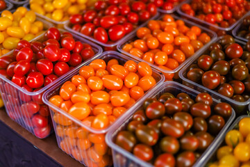 Fresh cherry tomatoes in containers are sold at the vegetable market, in different colors, yellow, brown, red, orange.