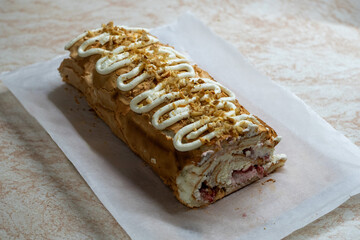 Close-up of a homemade meringue roll topped with whipped cream and chopped nuts, revealing layers of fluffy meringue, cream, and fresh berry filling. Photographed in soft natural light on parchment