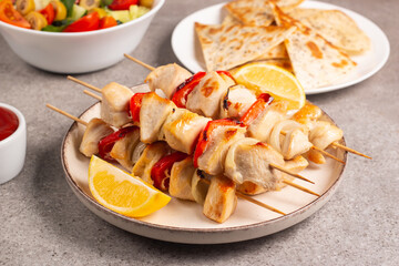 Delicious grilled chicken skewers with capsicum, lemon, salad and ketchup on a plate over the table. Chicken kebab. Healthy food concept.