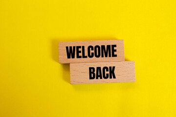 Welcome back message written on wooden blocks with yellow background. Conceptual welcome back symbol. Copy space.